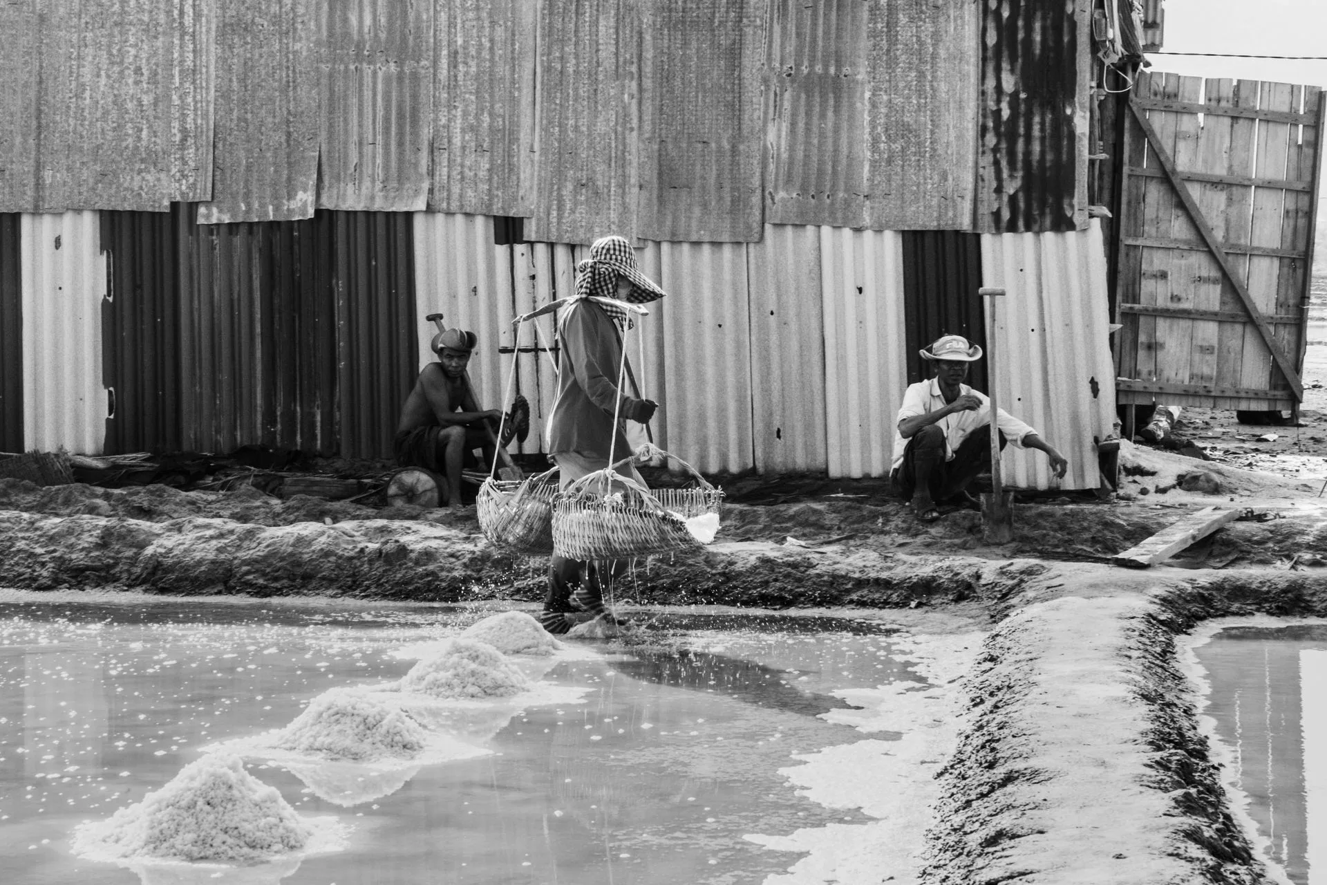 Black and white photo of workers carrying baskets across a salt field near Kampot