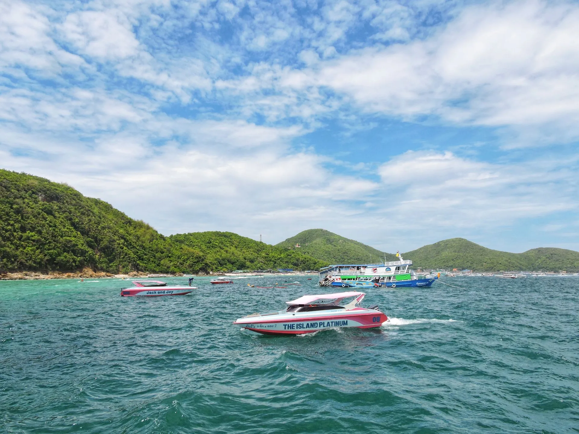 Speedboats and a ferry on turquoise water off the green hills of Koh Larn near Pattaya