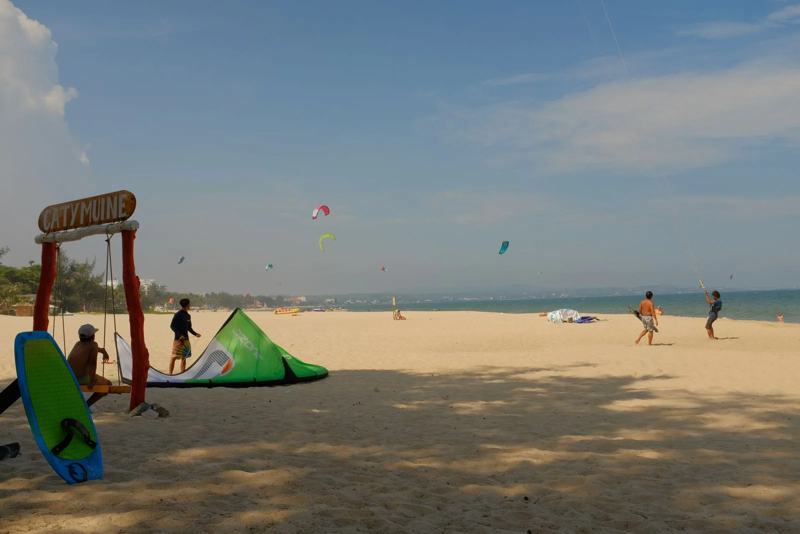 Kitesurfers rigging kites on a wide sandy beach in Mui Ne with colourful kites in the sky