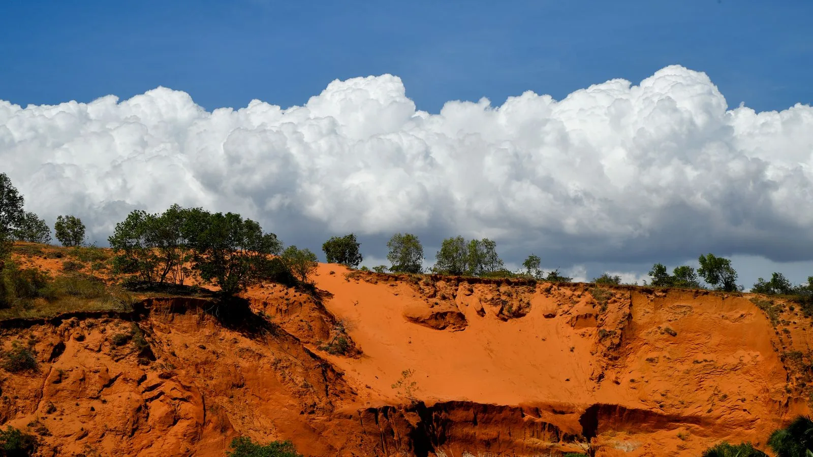 Eroded red sand cliffs near Mui Ne under a blue sky and towering white clouds
